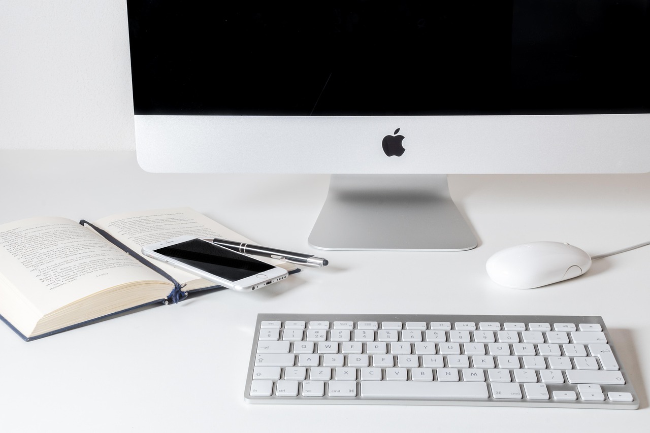 Escritorio de oficina con computadora, manzana, teléfono, libro y bolígrafo.
